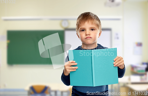 Image of displeased little boy with book at school