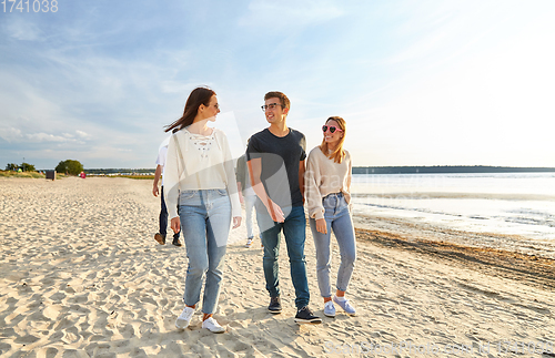 Image of happy friends walking along summer beach