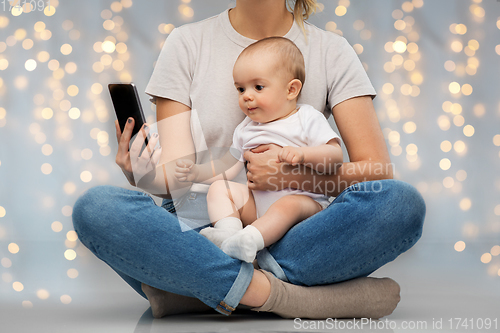 Image of mother and baby looking at smartphone over lights