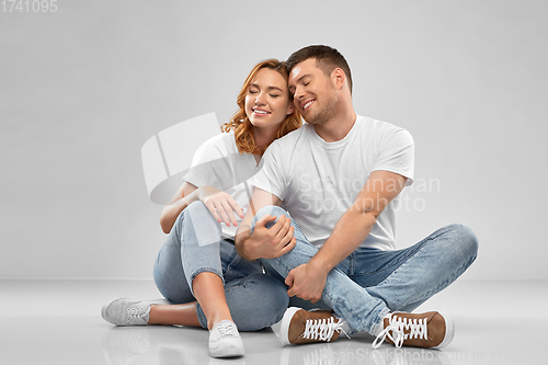 Image of happy couple in white t-shirts sitting on floor