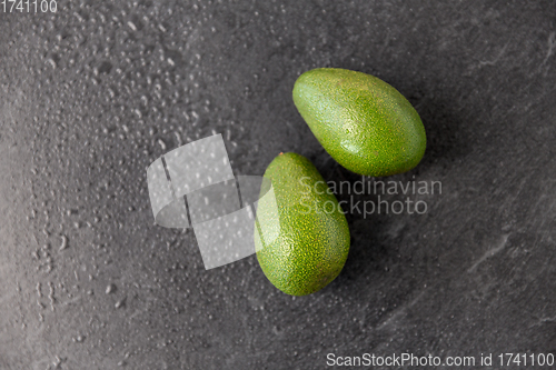 Image of two avocados on wet slate stone background