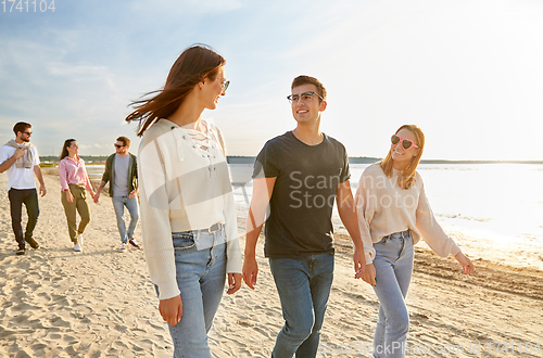 Image of happy friends walking along summer beach