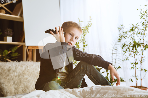 Image of Little boy using different gadgets at home