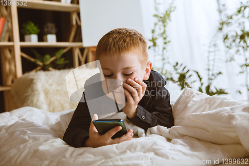 Image of Little boy using different gadgets at home