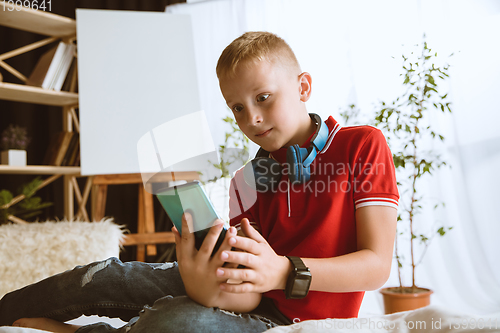 Image of Little boy using different gadgets at home