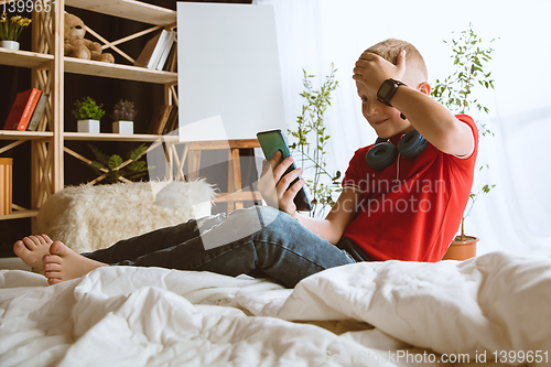 Image of Little boy using different gadgets at home