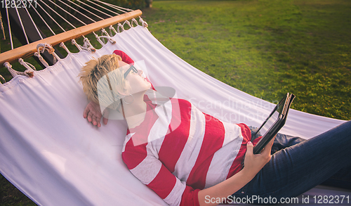 Image of woman using a tablet computer while relaxing on hammock