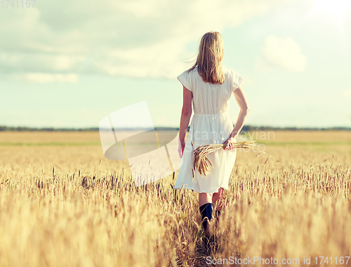 Image of young woman with cereal spikelets walking on field