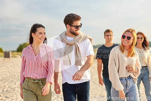 Image of happy friends walking along summer beach