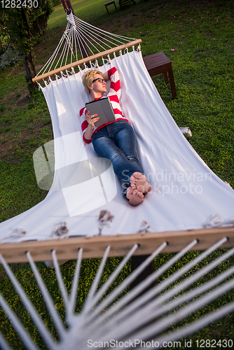 Image of woman using a tablet computer while relaxing on hammock