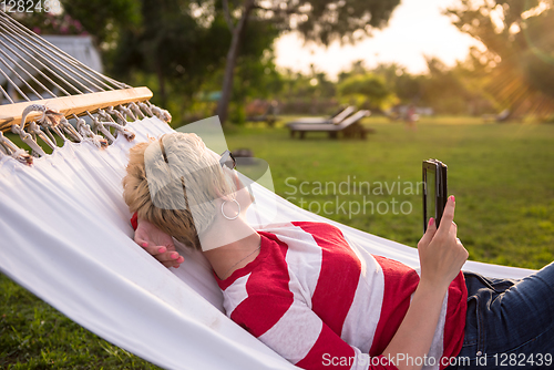 Image of woman using a tablet computer while relaxing on hammock