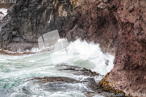 Image of ocean wave on a red rock at New Zealand