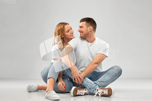 Image of happy couple in white t-shirts sitting on floor