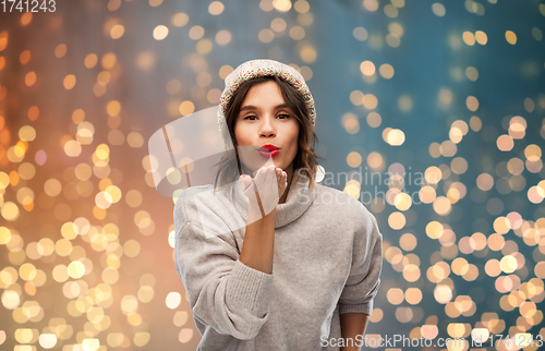 Image of young woman in knitted winter hat sending air kiss