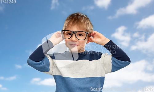 Image of portrait of smiling little boy in glasses over sky