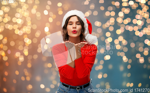 Image of happy young woman in santa hat sending air kiss