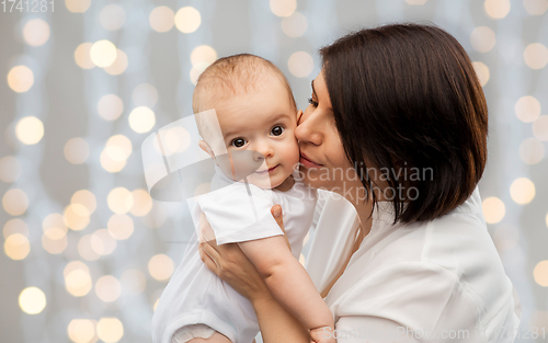 Image of happy mother kissing little baby over lights