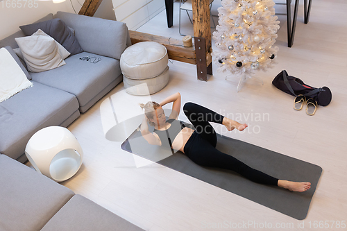 Image of Beautiful blonde woman doing home workout indoors. Woman practice yoga at home. Fit girl using workout tutorials for healthy active lifestyle. Woman using quarantine for home workouts.