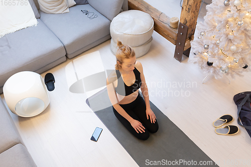 Image of Beautiful blonde woman doing home workout indoors. Woman practice yoga at home. Fit girl using workout tutorials for healthy active lifestyle. Woman using quarantine for home workouts.