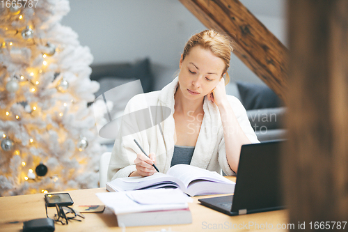 Image of Young female entrepreneur wearing cosy warm bathrobe working remotly from home in winter Christmas time during 2020 corona virus pandemic. Work from home, selter in place, concept.