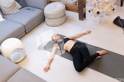 Image of Beautiful blonde woman doing home workout indoors. Woman practice yoga at home. Fit girl using workout tutorials for healthy active lifestyle. Woman using quarantine for home workouts.