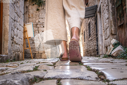 Image of Detail shot of female legs wearing comfortable travel sandals walking on old medieval cobblestones street dring sightseeing city tour. Travel, tourism and adventure concept