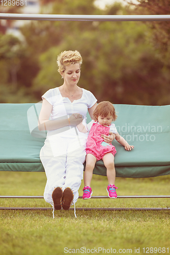 Image of mother and little daughter swinging at backyard