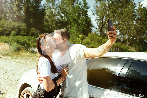 Image of Young couple making selfie near by car in sunny day