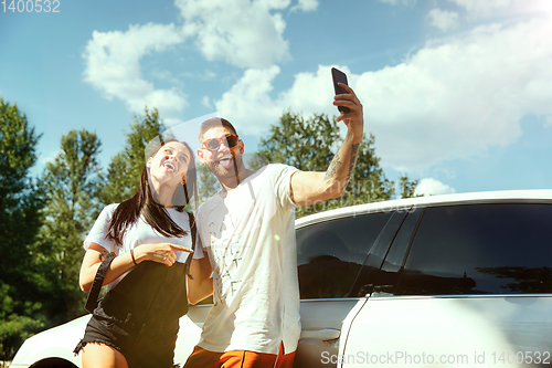 Image of Young couple making selfie near by car in sunny day