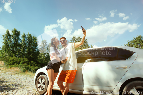 Image of Young couple making selfie near by car in sunny day