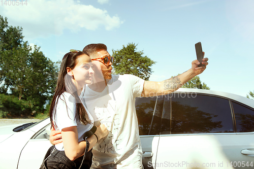 Image of Young couple making selfie near by car in sunny day