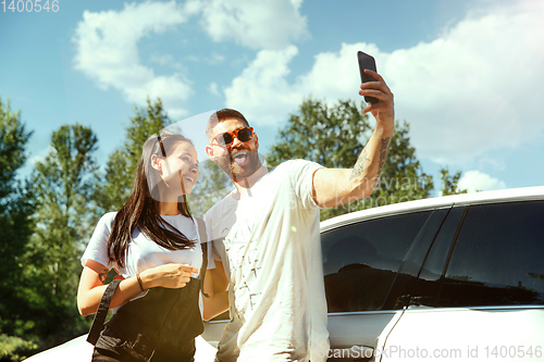 Image of Young couple making selfie near by car in sunny day