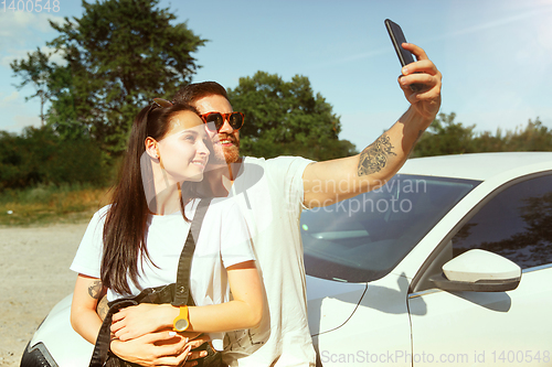 Image of Young couple making selfie near by car in sunny day