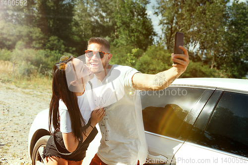 Image of Young couple making selfie near by car in sunny day