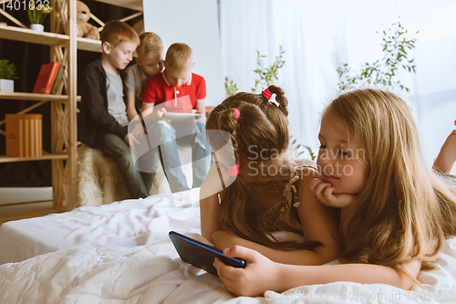 Image of Little boys and girls using different gadgets at home