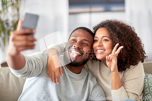 Image of happy couple with smartphone taking selfie at home