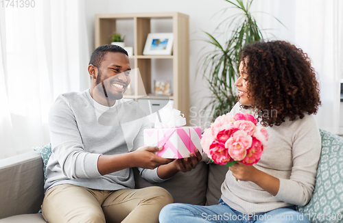 Image of happy couple with flowers and gift at home