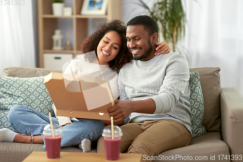 Image of happy african american couple eating pizza at home