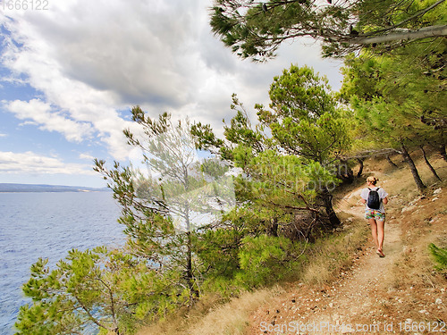 Image of Young active feamle tourist wearing small backpack walking on co