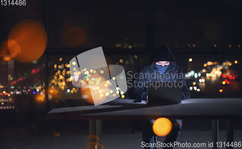 Image of hacker using laptop computer while working in dark office