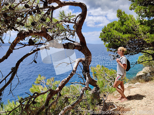 Image of Young active feamle tourist wearing small backpack walking on coastal path among pine trees looking for remote cove to swim alone in peace on seaside in Croatia. Travel and adventure concept