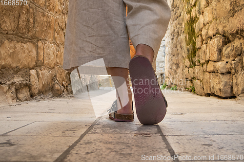 Image of Detail shot of female legs wearing comfortable travel sandals walking on old medieval cobblestones street dring sightseeing city tour. Travel, tourism and adventure concept