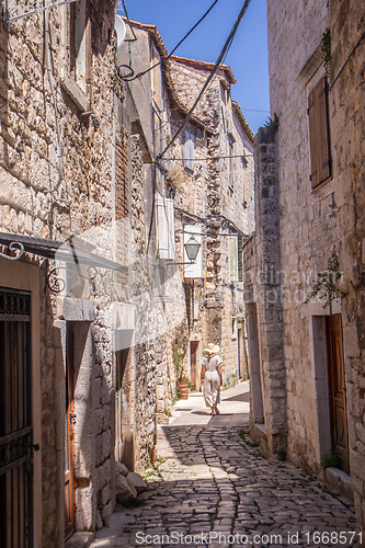 Image of Rear view of beautiful blonde young female traveler wearing straw sun hat sightseeing and enjoying summer vacation in an old traditional costal town at Adriatic cost, Croatia