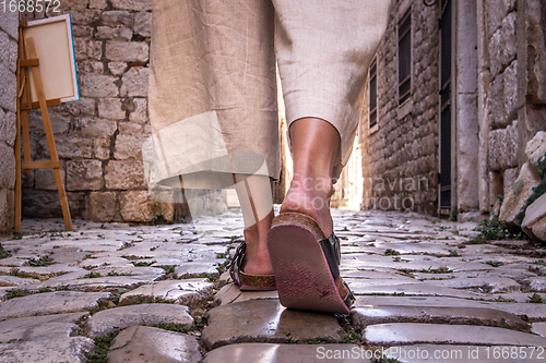 Image of Detail shot of female legs wearing comfortable travel sandals walking on old medieval cobblestones street dring sightseeing city tour. Travel, tourism and adventure concept