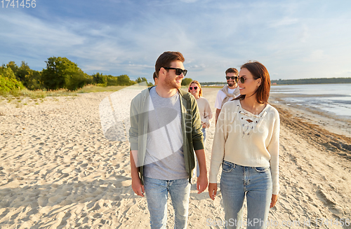 Image of happy friends walking along summer beach