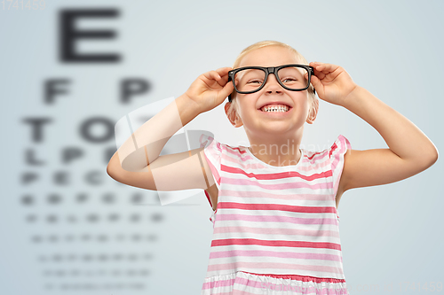 Image of smiling little girl in glasses over eye test chart