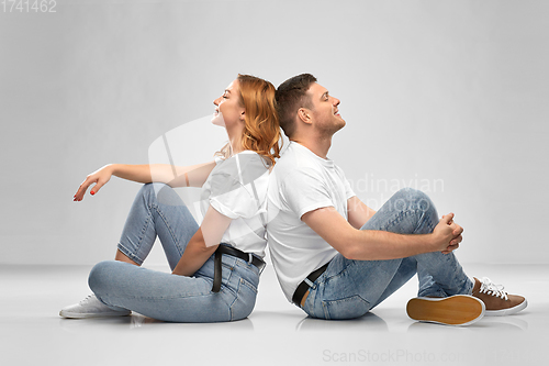 Image of happy couple in white t-shirts sitting on floor