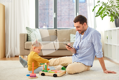 Image of father with smartphone and baby daughter at home