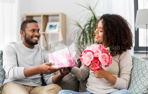 Image of happy couple with flowers and gift at home