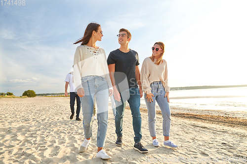 Image of happy friends walking along summer beach